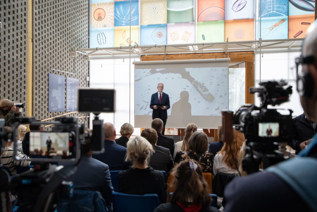 Statsminister Jonas Gahr Støre på scenen foran kameraer og folk på Universiteter i Tromsø. Fotograf Jørn Berger-Nyvoll / UiT