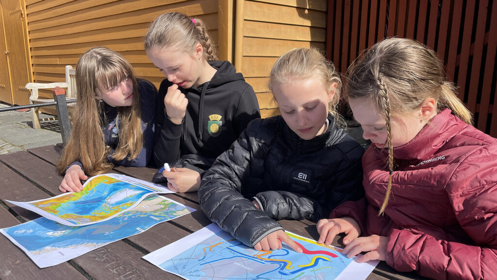 Fire elever sitter ved et bord og ser på kart som ligger foran dem